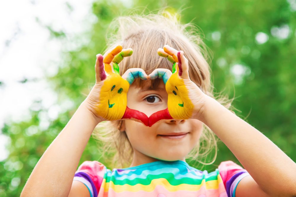 Child hands in heart shape covered with finger paint colors.